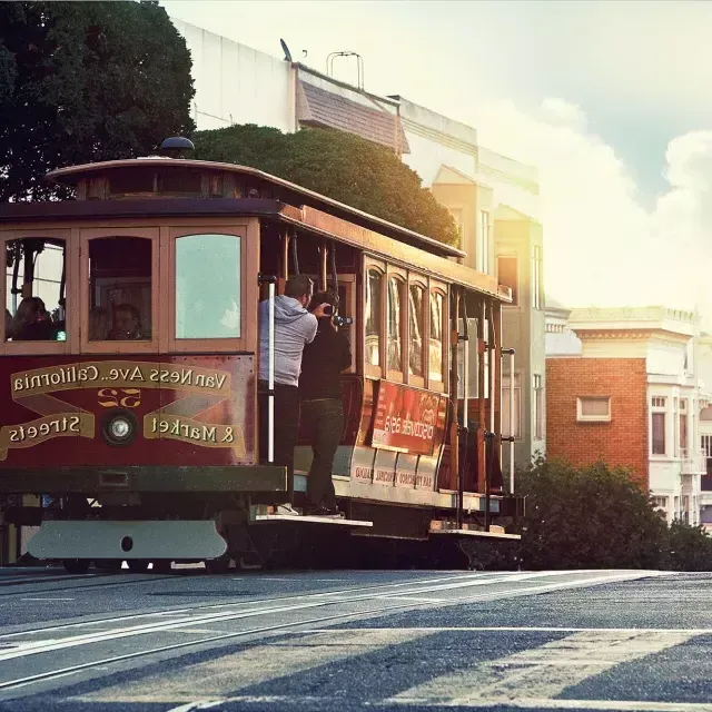 A cable car rounds a hill in San Francisco with passengers looking out the window.